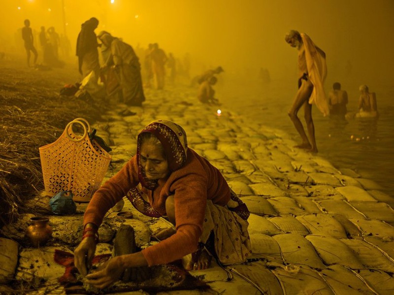 25 На рассвете, во время Маха Кумбха Мела (религиозного фестиваля Индии) пожилая женщина выполняет пуджу – приносит ритуальную жертву богам. Автор - Alex Webb.