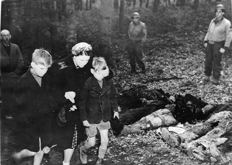 21  Мать-немка закрывает глаза сыну, когда они проходят мимо эксгумированных тел 57 русских солдат, 3 мая 1945 года.