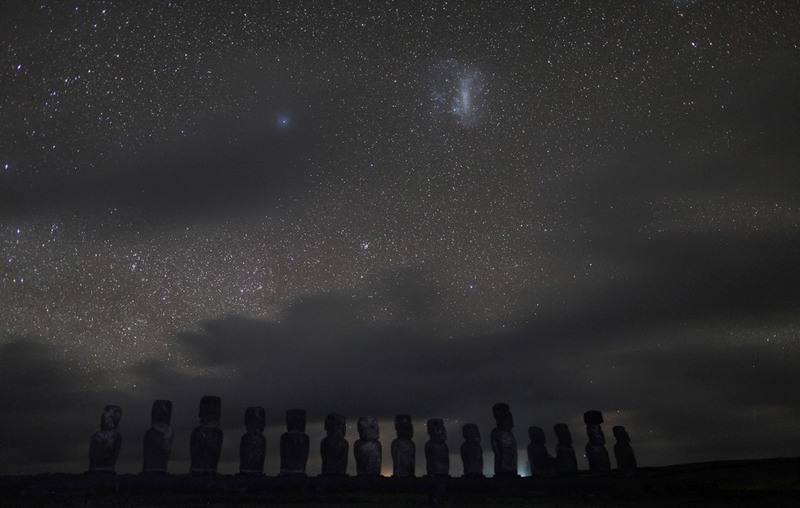 2. Снимок сделан в ночное время над силуэтами древних статуй Моаи на острове Пасхи. На небе видна ярая туманность –  Большое Магелланово Облако.