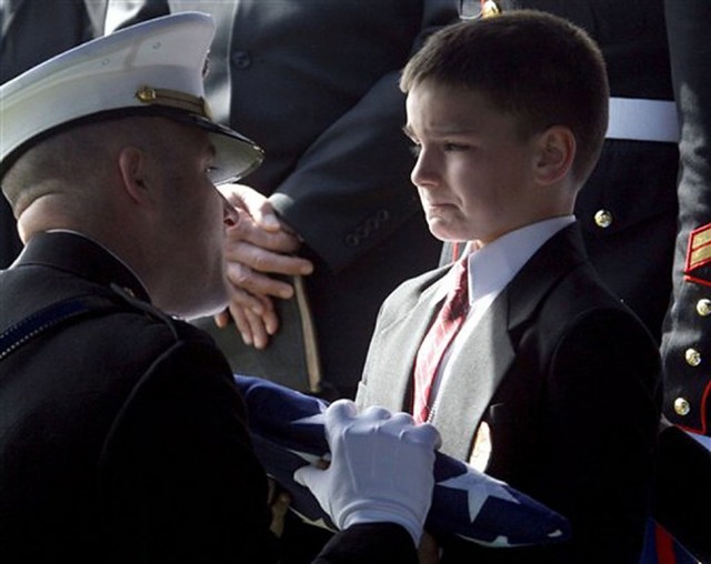 Восьмилетний Кристиан принимает флаг во время поминальной службы по его отцу. Отец был убит в Ираке всего за пару недель до того, как должен  был вернуться домой.