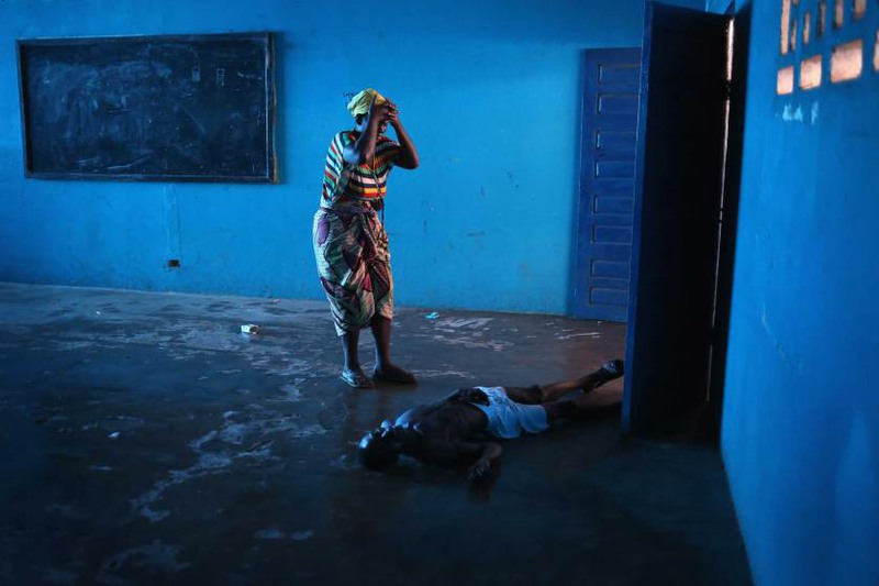 3  Автор - JOHN MOORE—GETTY IMAGES. Umu Fambulle stands over her husband Ibrahim after he staggered and fell knocking him unconscious, in an Ebola ward in Monrovia, Liberia., Aug. 15, 2014.