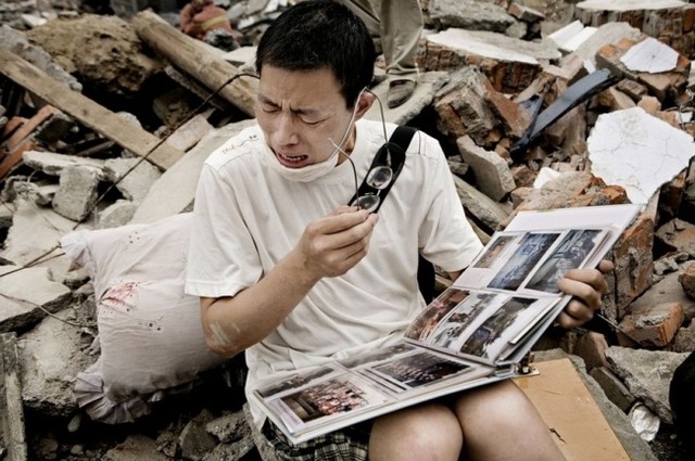 Человек смотрит семейный альбом, который нашел в щебне своего старого дома, после землетрясения в Сычуани.